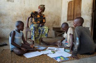 A woman helps boys with schoolwork, part of IRC programs of child protection